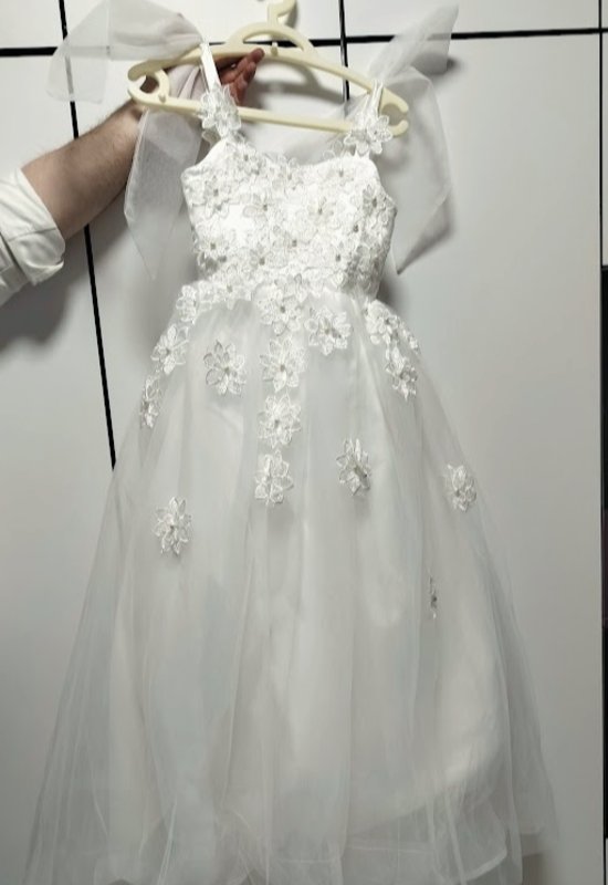 שמלת כלה חדשה (ללא שרוולים). 
חלק עליון אפליקציות פרחים עם סרטי אורגנזה גדולים על הכתפיים, חלק תחתון טול.
מתאים בערך לגיל 7, נמכרת עקב טעות במידה